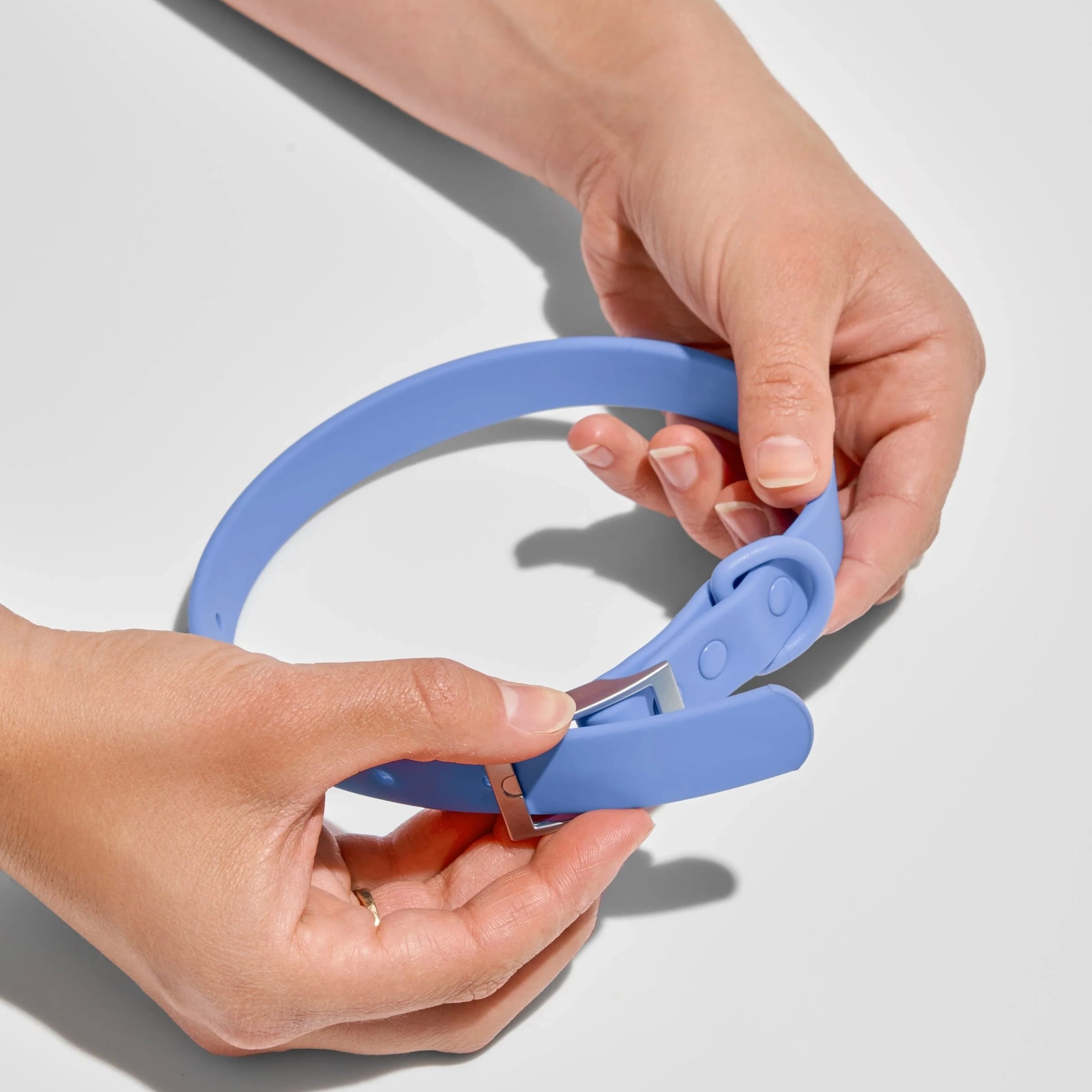 Hand holding a sky blue MoonianPet waterproof PVC-coated dog collar — zinc alloy hardware resists corrosion after repeated swimming and water exposure